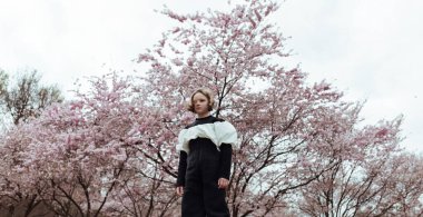 Duygusuz küçük kızın düşük açılı görüntüsü parkta çiçek açan kiraz ağacının yanında duruyor.