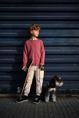 Uzun boylu kaykaycı ve tasmalı sadık köpek bina duvarının yanında dinlenirken gözlerini kaçırıyor.