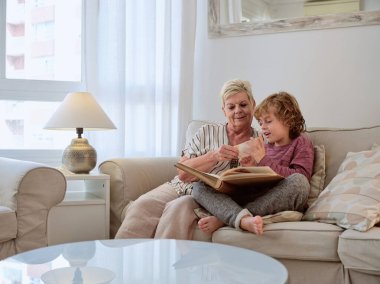 Olumlu çocuk ve yaşlı kadın evdeki rahat oturma odasında, lambanın yanındaki kanepede dinlenirken inanılmaz bir fotoğrafa bakıyorlar.