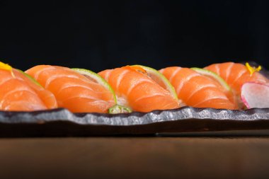 Tepside servis edilen somonlu taze nigiri suşisi ve siyah arka planda limon ve çiçeklerle süslenmiş.