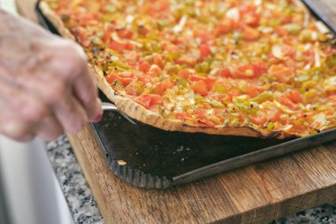 Ekin bayanının aşçılığı, iştah açıcı vejetaryen pizzayı mutfak tahtasının üzerinde dilimliyor.