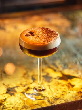 Barda servis edilen kahve çekirdekleri ve beyaz köpüklü kakao tozuyla süslenmiş alkollü espresso martini kokteyli.