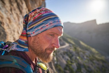Sırt çantalı, duygusuz, orta yaşlı bir adamın portresi. Resimli dağlık arazide duruyor.