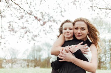 Parktaki ağacın altında dikilirken siyah bluzlu, sarı saçlı mutlu kadın sarılıyor.
