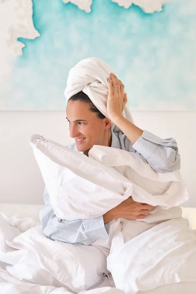 Szczęśliwa Młoda Kobieta Ręcznikiem Owiniętym Wokół Głowy Obejmująca Poduszki Siedząc — Zdjęcie stockowe