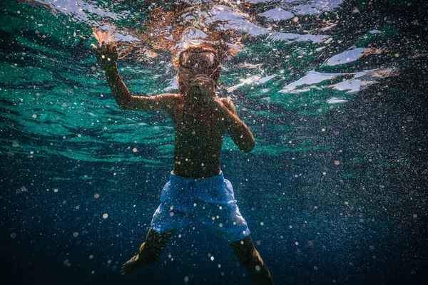 白のショートパンツとターコイズブルーの下で泳ぐシュノーケリングマスクの10代の子供は泡で海水を波打つ — ストック写真