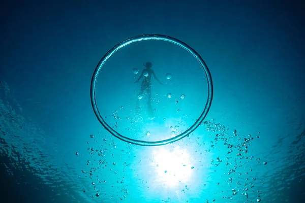 Underwater shot of big bubble ring against boy diving in deep blue ocean during vacation