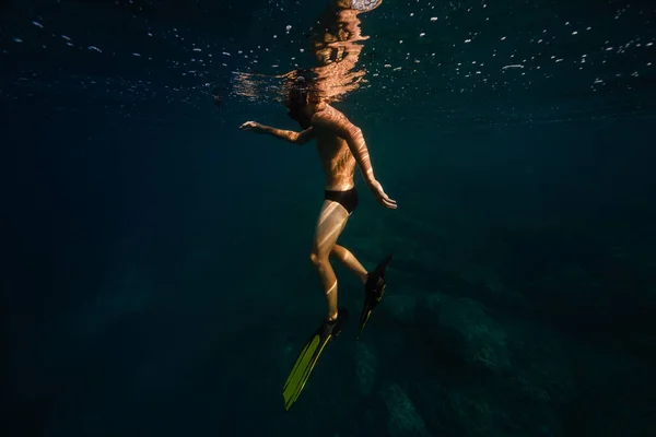 サイドビュー 晴れた日に深海の青い水の下に浮かぶスリッパとゴーグルで認識できないシャツレスの男性ダイバーのフルボディ — ストック写真