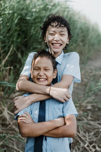 Веселий Азіатський Хлопчик Обіймає Молодшого Брата Шкільній Формі Посміхаючись Дивлячись — стокове фото