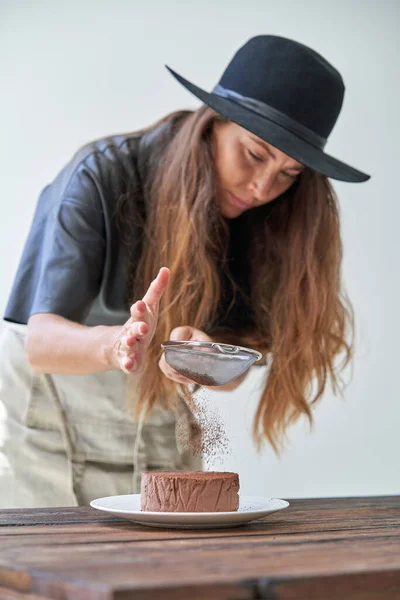 Латиноамериканка Шляпе Длинными Волосами Стоящая Деревянным Столом Украшающая Торт Шоколадным — стоковое фото