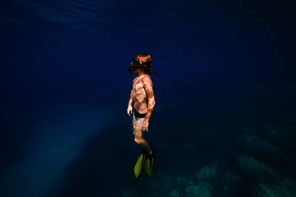 休暇中に深海の濃い青い水の下でスリッパとシュノーケリングマスクダイビングで10代のシャツレスの男の子のサイドビュー — ストック写真
