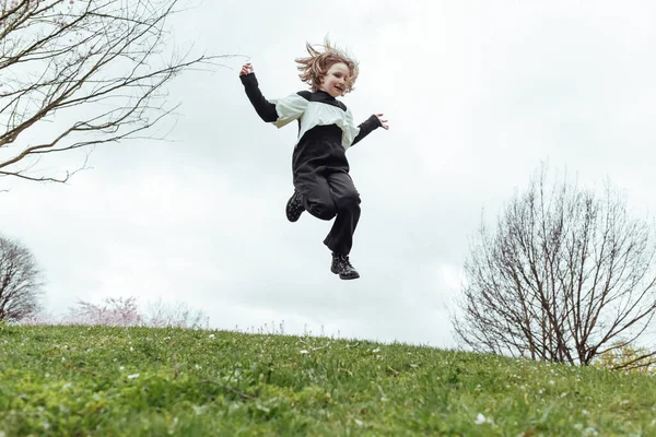 緑の草の丘にジャンプ黒と白の衣装で幸せな19歳の少女のフルボディの下から — ストック写真