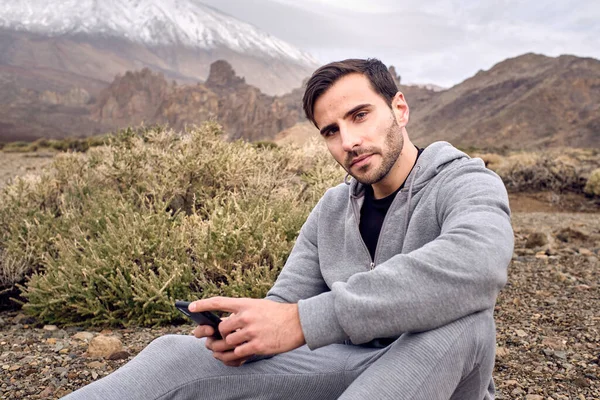 Schöner Bärtiger Mann Aktivkleidung Mit Handy Während Auf Steinigem Grasbewachsenem — Stockfoto