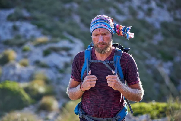山の中の丘のぼやけた背景に晴れた日に岩の道を歩くバックパックを持つ成熟したひげそりの男性ハイカー — ストック写真