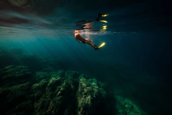 荒いサンゴ礁の近くの深海の青い水の下で泳ぐフリッパーダイバーの匿名のダイバーのサイドビュー — ストック写真