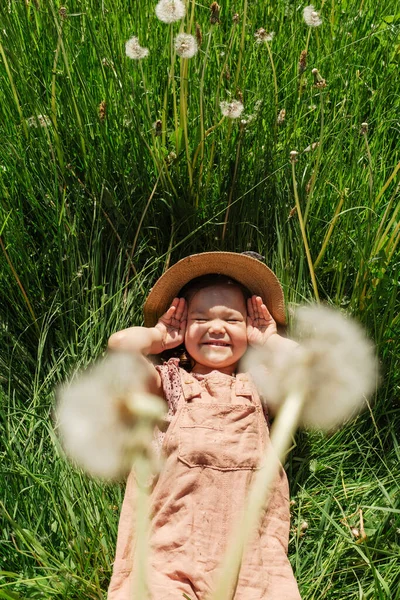 화창한 민들레와 초원에 모자와 전체를 착용하는 장난스러운 소녀의 위에서 — 스톡 사진