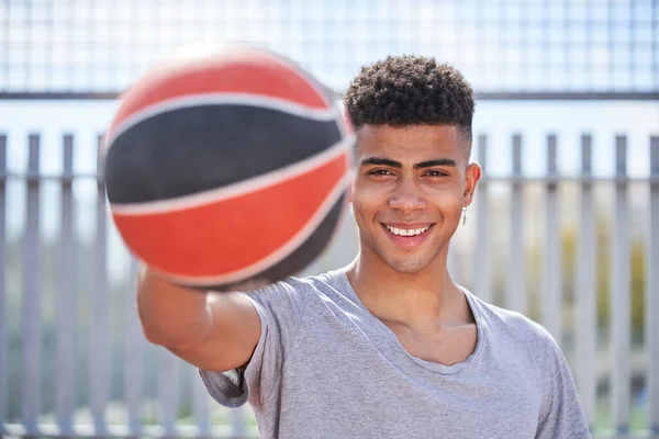 Spor kıyafetleri içinde spor sahasında durup elinde basketbol topu tutarken gülümseyen ve kameraya bakan Afro-Amerikan erkek sporcu.