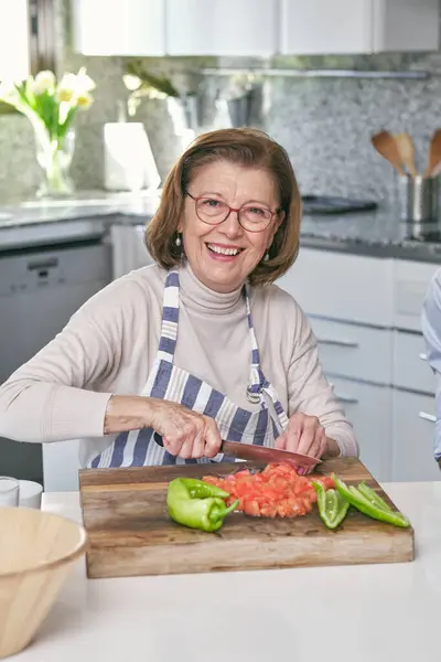 Önlüklü Yaşlı Bir Kadın Gülümseyerek Kameraya Bakarken Mutfaktaki Ahşap Kesme — Stok fotoğraf