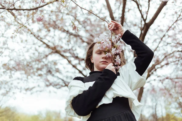 少女静静地站在盛开的树下 闭着眼睛 牵着树枝在公园里 — 图库照片