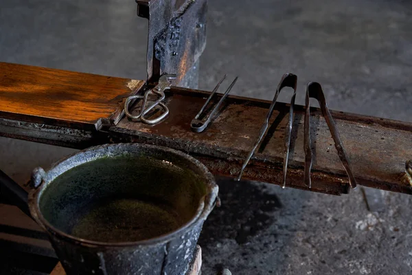 ガラス造りの工場の水で満たされるバケツの近くの木のベンチのさまざまなガラス吹く古い用具 — ストック写真