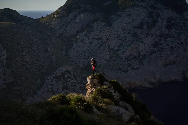 岩の端に立つ匿名の男性ハイカーと日没時に山と絵のような風景を賞賛 — ストック写真