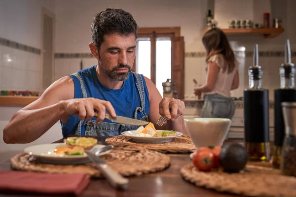 Hombre Barbudo Enfocado Comiendo Apetitosos Huevos Revueltos Mientras Mujer Cocina — Foto de Stock