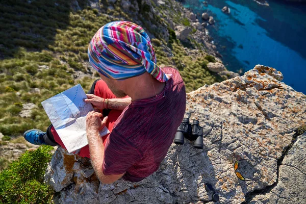 夏の旅行中に岩の多い山の崖に座っている間 バンダナの認識できない旅行者の上から地図をチェック — ストック写真