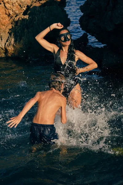 无名小卒身穿泳衣 戴着潜水面具 一边在海里玩乐 一边往妈妈身上泼水 — 图库照片