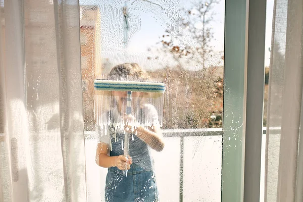 家事をするカジュアルな服の匿名の子供の窓や自宅でバルコニーにモップで窓を掃除する — ストック写真