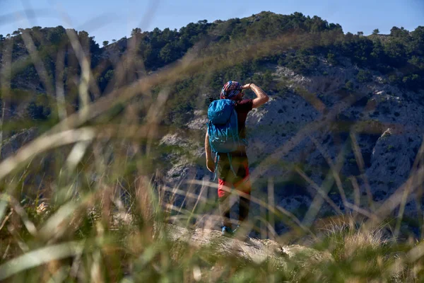 男性ハイカーのフルボディバックパック草の山の斜面に立って 晴れた日に離れて見て — ストック写真