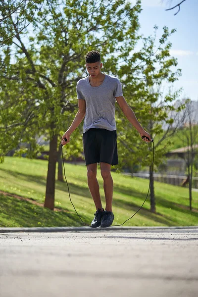 太陽の下で緑の芝生に対してアスファルト舗装にロープをジャンプとスポーツウェアの訓練でヒスパニック男性の完全な体 — ストック写真