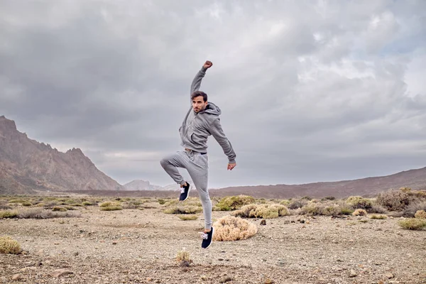 スポーツウェアを着た陽気な男性の全身は 曇った日にスペインのテネリフェ島の山Teideの火山地帯の近くの乾燥した地面にジャンプします — ストック写真