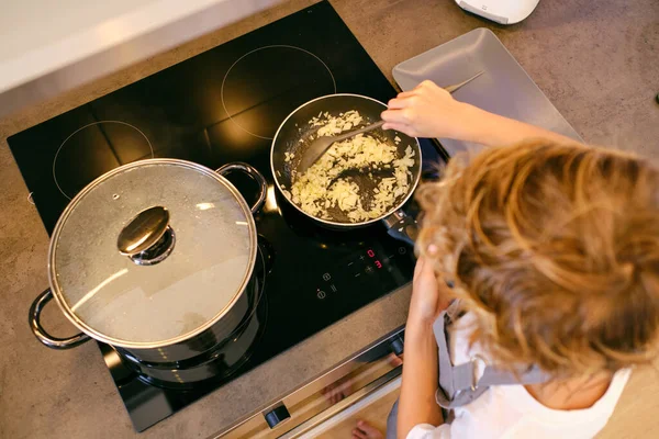 キッチンで調理中にストーブの上でフライパンに玉ねぎを攪拌スプーンヘラで作物匿名人の高角度 — ストック写真