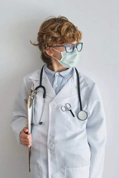 Marzycielskie Dziecko Mundurze Medycznym Masce Oddechowej Schowkiem Odwracając Wzrok Białym — Zdjęcie stockowe