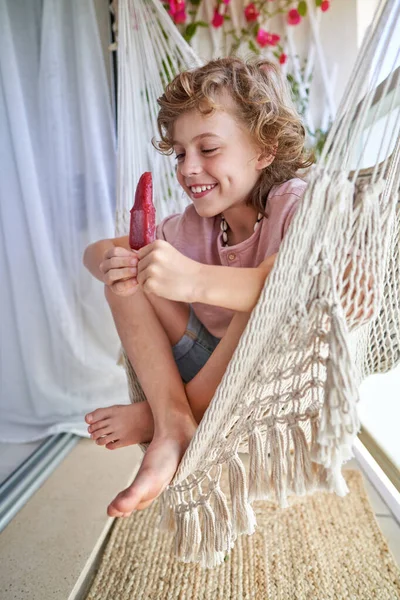 穿着休闲装的快乐 无忧无虑 可爱的孩子 一边微笑着 一边看着红色的冰棍 一边在白天坐在吊床上 — 图库照片