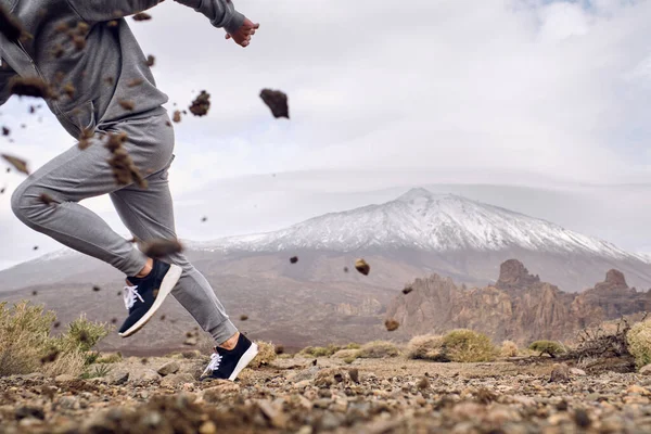 スペインのカナリア諸島のテネリフェ島にあるTeide火山の近くの汚い石の地面で速く走るスポーツウェアやスニーカーの作物の匿名の男性の側面図 — ストック写真