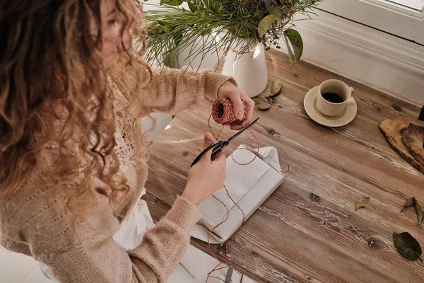 在家里准备节日庆祝活动的时候 一个难以辨认的有创意的女人站在桌旁 手里拿着包着礼物的咖啡和装饰品 — 图库照片