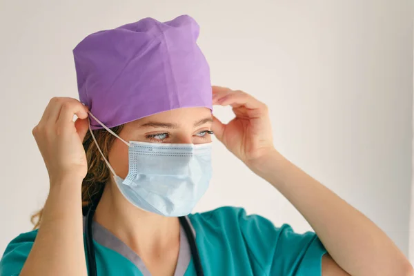 医療制服を着たプロの女性医師が保護マスクをつけ ベージュの背景を離れて見ます — ストック写真
