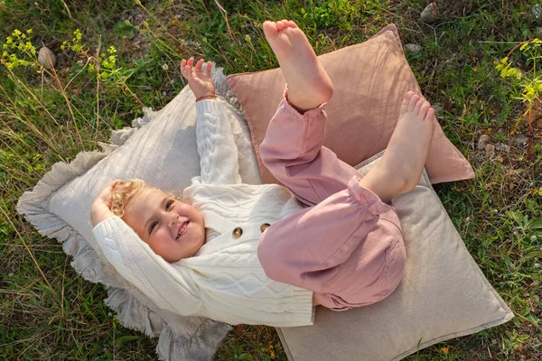 Shora Usměvavá Holčička Stylovém Oblečení Ležící Nohama Zvednutýma Měkkých Polštářích — Stock fotografie