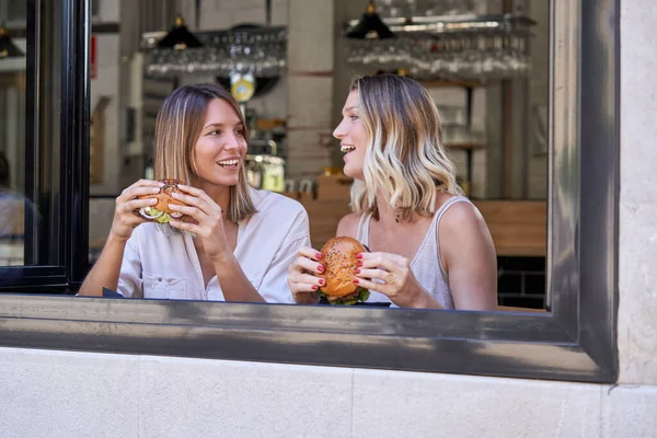 愉快的女士们坐在窗边的咖啡店里 一边吃着美味的汉堡包 一边相互凝视着 一边享受着相见的乐趣 — 图库照片