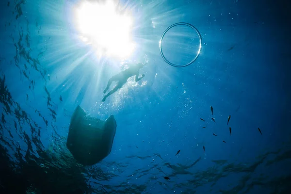 カタマラン近くの深海でシュノーケリングをしている匿名の子供の水中ビューからと活気のある太陽光線の下で表面上のリングバブル — ストック写真