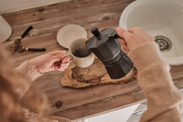 上から作物の無名の女性で暖かいセーターに熱いコーヒーを注ぐから間欠泉コーヒーメーカーにカップでキッチン — ストック写真