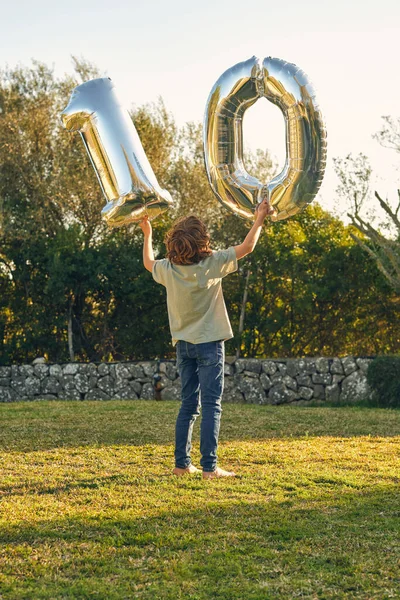 戻る誕生日を祝いながら芝生の芝生の上に立つ数10の形の風船と認識できない少年の完全な体を表示します — ストック写真