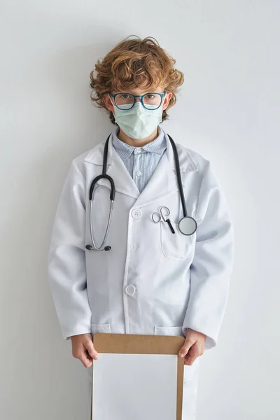 Dziecko Okularach Szlafroku Medycznym Jednorazową Maską Pustą Kartką Papieru Patrzące — Zdjęcie stockowe