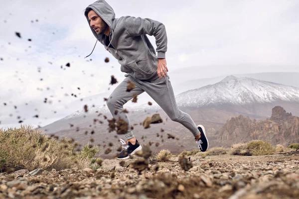 サイドビュー山に対して速く走るスポーツウェアで焦点を当てたヒスパニック男性アスリートの完全な長さの地面レベルテネリフェ島で石を投げ捨てるカナリア島スペイン — ストック写真