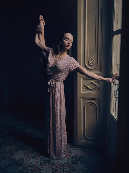 足を上げて目を閉じている間 暗い部屋のドアに対して立っている長いドレスのフルボディバレリーナ — ストック写真