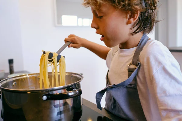 在厨房的炉子上用勺子在平底锅上做意大利面的作物惊喜儿童侧视图 — 图库照片