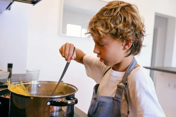 Πλάγια Άποψη Του Εξυπηρετικού Παιδιού Ποδιά Σπάτουλα Μαγείρεμα Ζυμαρικά Κατσαρόλα — Φωτογραφία Αρχείου