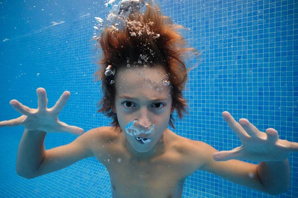 深刻な男の子とともにぬれた髪を怖がらせますと吹いて空気泡でプールで澄んだ水とカメラを見て — ストック写真
