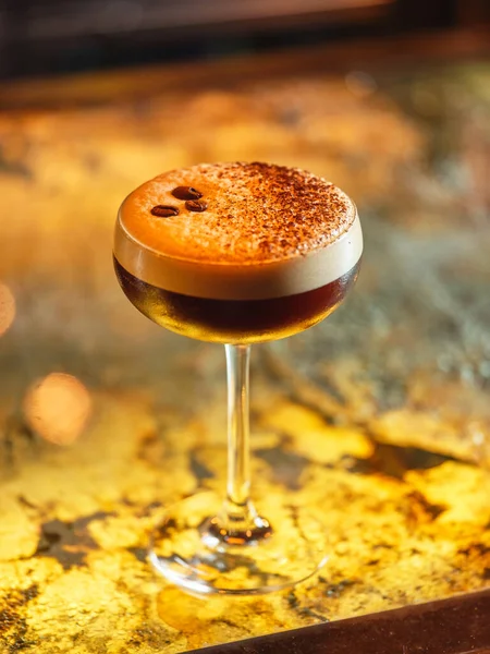 Barda servis edilen kahve çekirdekleri ve beyaz köpüklü kakao tozuyla süslenmiş alkollü espresso martini kokteyli.